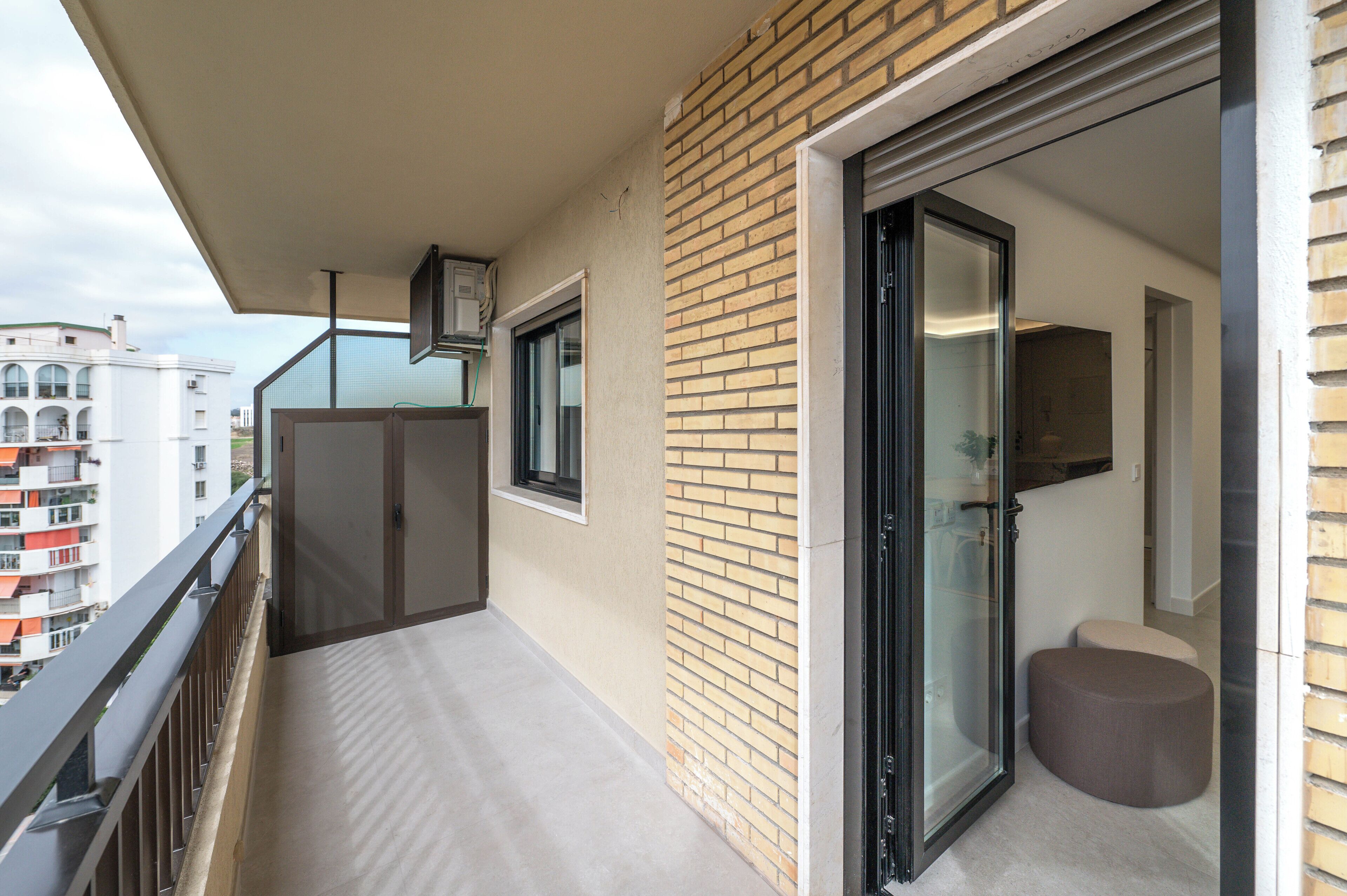 A balcony with a glass door, a small seating area, and a view of other buildings.