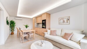 A modern living space with a dining area, kitchen, and a white sofa with cushions. - LXR Dalí 1-Bedroom Beachfront (Fuengirola)