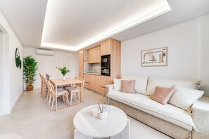 A modern living space with a dining area, kitchen, and a white sofa with cushions. - LXR Dalí 1-Bedroom Beachfront (Fuengirola)