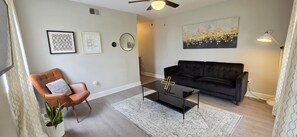 Un salon avec un canapé noir, un fauteuil en cuir marron, une table basse et un grand tableau abstrait accroché au mur.