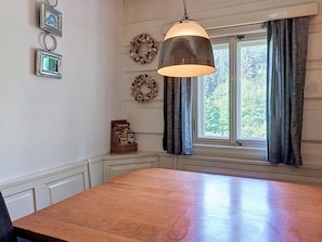 Une cuisine avec une table en bois, un luminaire suspendu et une fenêtre avec des rideaux.