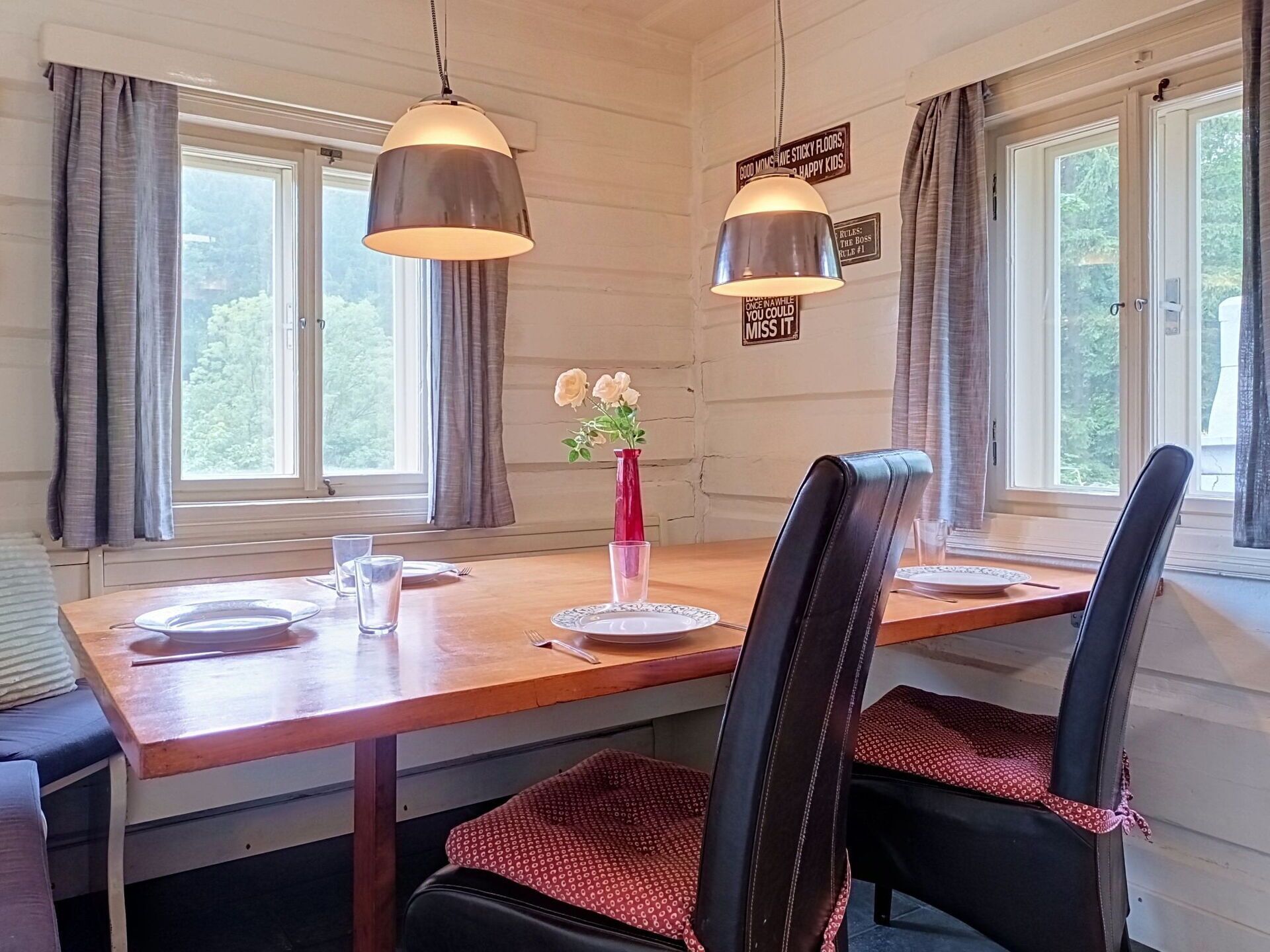 A dining area with a wooden table, two chairs, a vase with flowers, and two pendant lights.