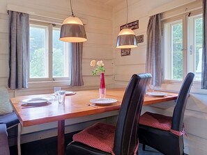 A dining area with a wooden table, two chairs, a vase with flowers, and two pendant lights.