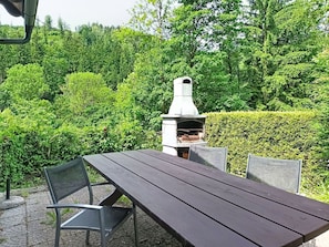 Une terrasse extérieure avec une table et des chaises en bois, un sol carrelé en pierre et un four extérieur en pierre.
