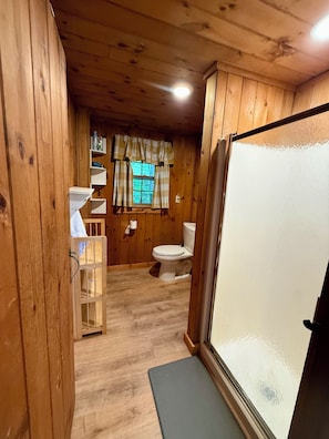 Ein Badezimmer in einer Holzhütte mit Toilette, Waschbecken und einem Fenster mit Vorhängen.