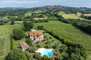 Una villa con piscina circondata da vigneti, immersa in un paesaggio collinare con un paese in lontananza.