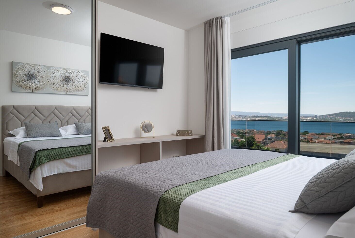 Une chambre d’hôtel moderne dotée de deux lits, d’un téléviseur à écran plat, d’une grande fenêtre offrant une vue sur la ville et d’un décor minimaliste.