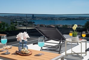 Eine Dachterrasse mit einem Tisch für zwei Personen, einem Stuhl, einer Blumenvase und zwei Gläsern blauer Cocktails.