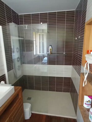 Ein modernes Badezimmer mit einer ein Glaswand abschirmenden Dusche, einem weißen Waschbecken und einem Holzwaschtisch.