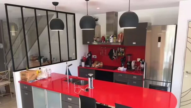 A modern kitchen with a red countertop, black chairs, and pendant lighting. - Quiet house in the middle of fields 15 min from Bayeux, 30 from the landing beaches (Aurseulles)