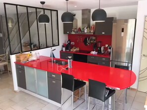 A modern kitchen with a red countertop, black chairs, and pendant lighting.
