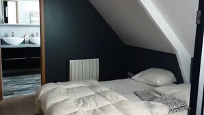 A bedroom with a sloped ceiling, a bed with white bedding, a headboard, and a large mirror above a vanity with two sinks. - Quiet house in the middle of fields 15 min from Bayeux, 30 from the landing beaches (Aurseulles)
