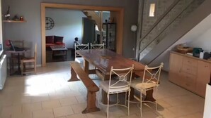 A spacious dining area with a long wooden table and white metal chairs, a kitchen with cabinets, and a staircase. - Quiet house in the middle of fields 15 min from Bayeux, 30 from the landing beaches (Aurseulles)