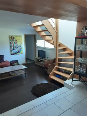 Ein Wohnzimmer mit Wendeltreppe, Flachbildfernseher, Sofa und einem Gemälde an der Wand.
