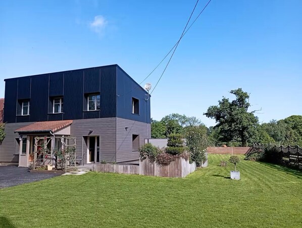 Uma casa moderna de dois andares com telhado plano, varanda frontal e gramado bem cuidado.