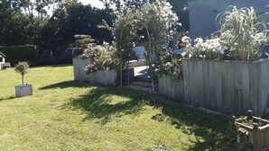 A residential garden with a wooden fence, a small tree, and flowering plants. - Quiet house in the middle of fields 15 min from Bayeux, 30 from the landing beaches (Aurseulles)