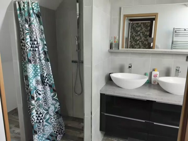 A bathroom with two white sinks, a shower, and a patterned curtain.