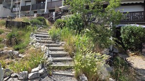 A multi-story building with balconies, a stone staircase leading to the entrance, and surrounding vegetation. - Cosy studio with terrace (Gréolières)