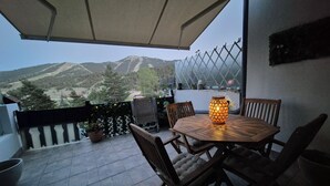 A balcony with a table and chairs, a decorative lantern, and a view of a mountainous landscape. - Cosy studio with terrace (Gréolières)