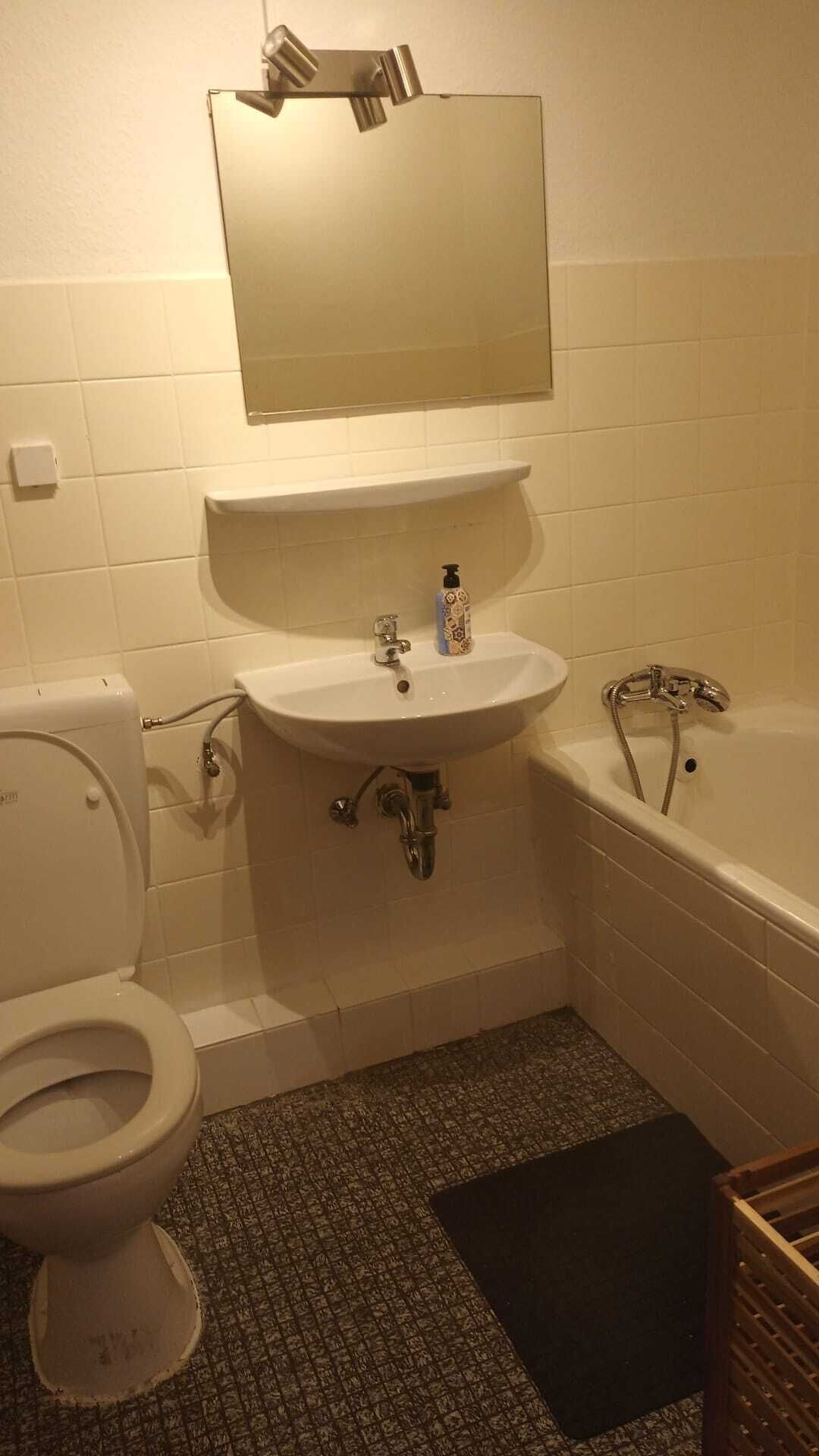 A bathroom with a toilet, sink, mirror, and bathtub.