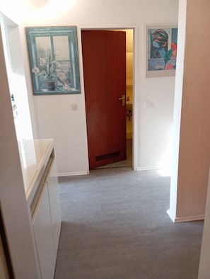 A hallway with a wooden door, a potted plant, and a framed picture on the wall.