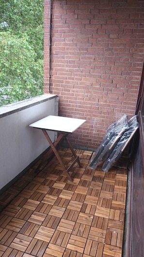 A balcony with a wooden floor, a white table, and a brick wall.