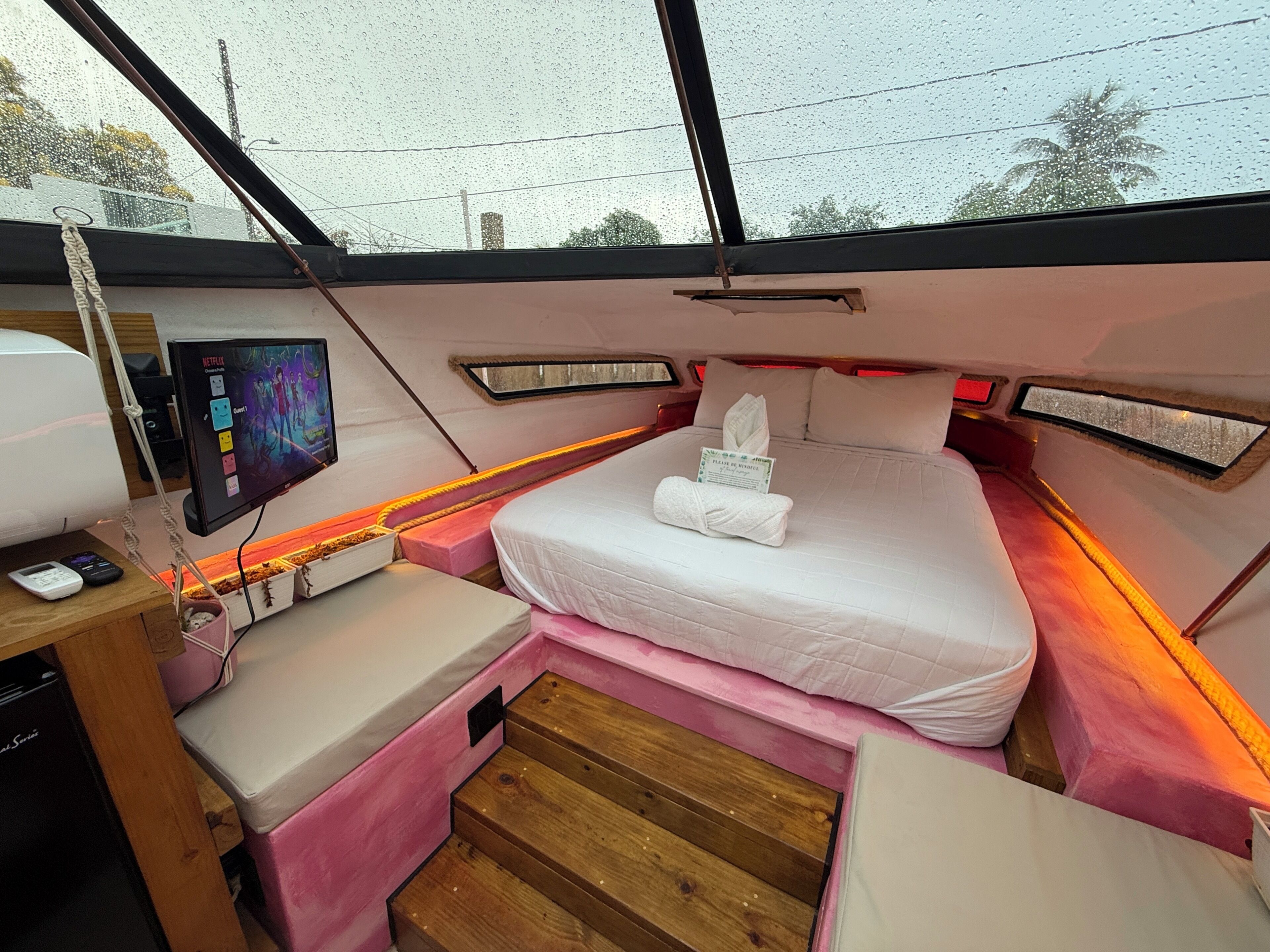 A compact room with a bed, a small desk with a computer, and a window with a view of trees.