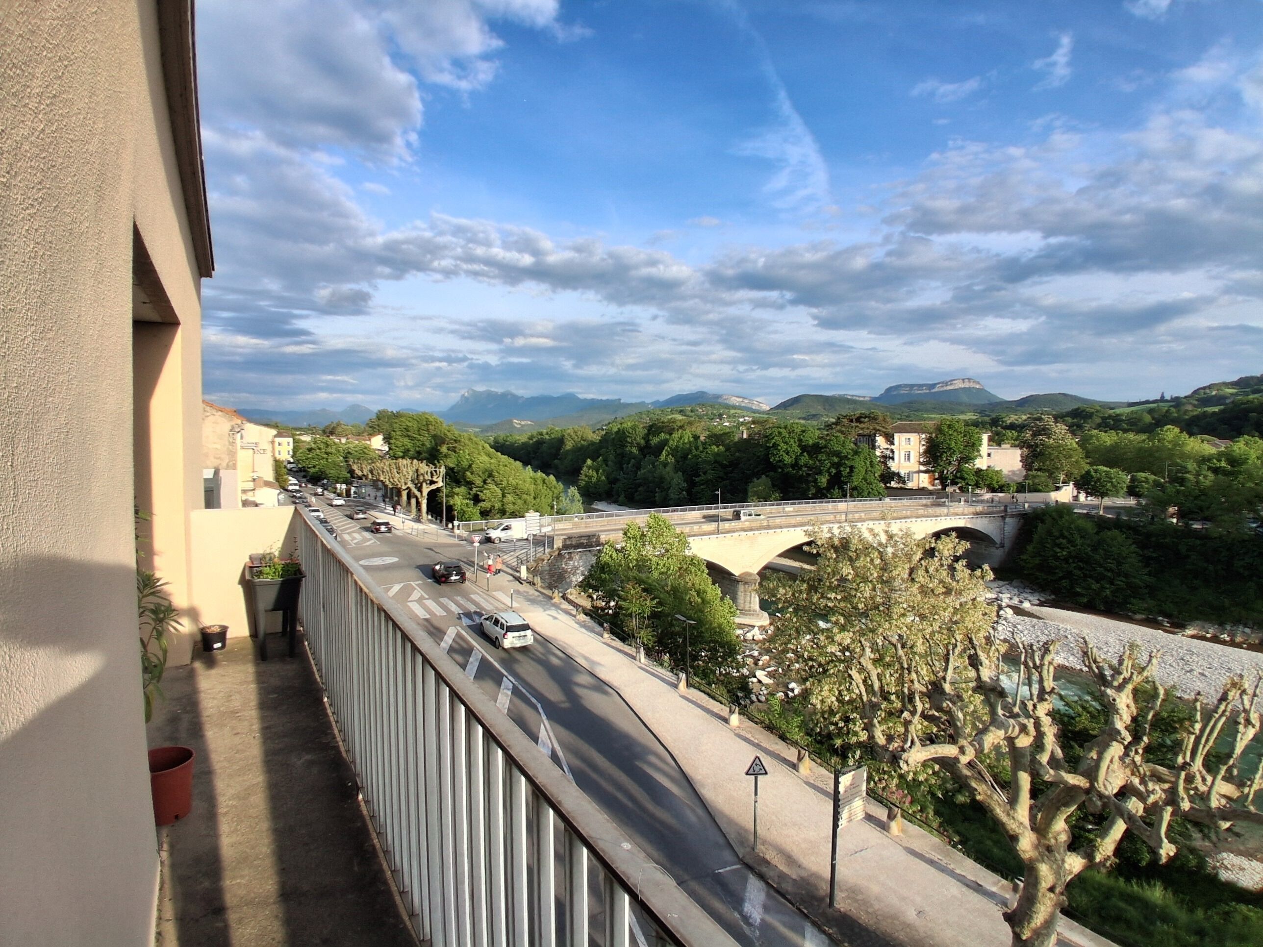 A balcony overlooking a road with a bridge, greenery, and distant mountains.