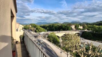 A balcony overlooking a road with a bridge, greenery, and distant mountains.