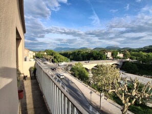 A balcony overlooking a road with a bridge, greenery, and distant mountains.