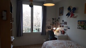 Une chambre à coucher comprenant un lit, un bureau avec une chaise, une fenêtre avec des rideaux et des éléments de décoration murale.