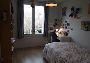 Ein Schlafzimmer mit einem Bett, einem Schreibtisch mit Stuhl, einem Fenster mit Vorhängen und Wanddekorationen.