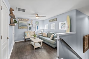 Un salon comprenant un canapé, une table basse et des éléments de décoration murale, notamment une planche de surf et des tableaux encadrés.