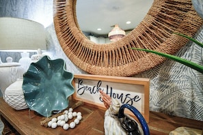 Una mesa de madera con un letrero que dice 'Beach House', objetos decorativos y un tapiz tejido.