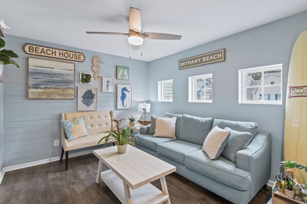 A living room with a light blue wall, a ceiling fan, a sofa, a coffee table, and framed artwork.