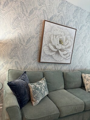 Un salon avec un canapé vert, une grande œuvre d’art florale et un papier peint à motifs.