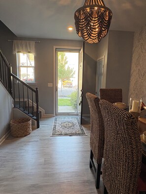 A staircase leading to a door, a wicker chair, a rug, and a chandelier.