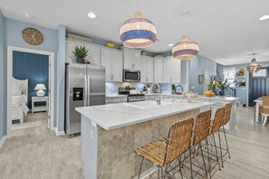 A modern kitchen with a central island, stainless steel appliances, and a dining area with wicker chairs.