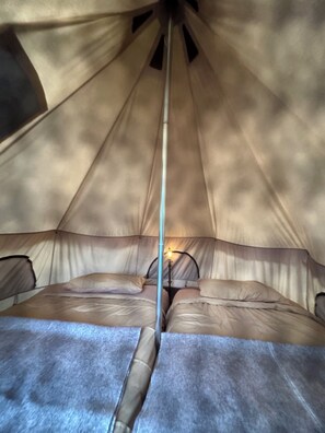 A tent with a central pole, two beds with pillows, and a small table with a light.