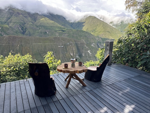 A wooden deck with a table and chairs overlooking a mountainous landscape.