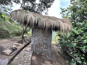 A stone structure with a thatched roof, surrounded by greenery and a stone pathway.
