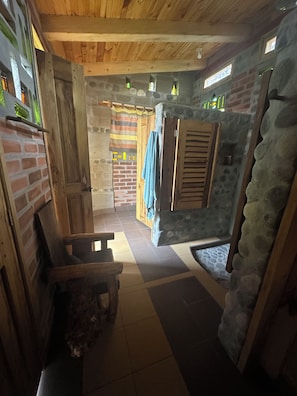 A rustic interior with a wooden ceiling, stone walls, a tiled floor, and a wooden bench.