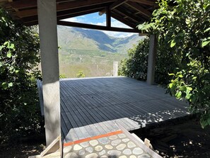 Un espacio al aire libre cubierto con piso de madera, rodeado de vegetación y vistas a un paisaje montañoso.