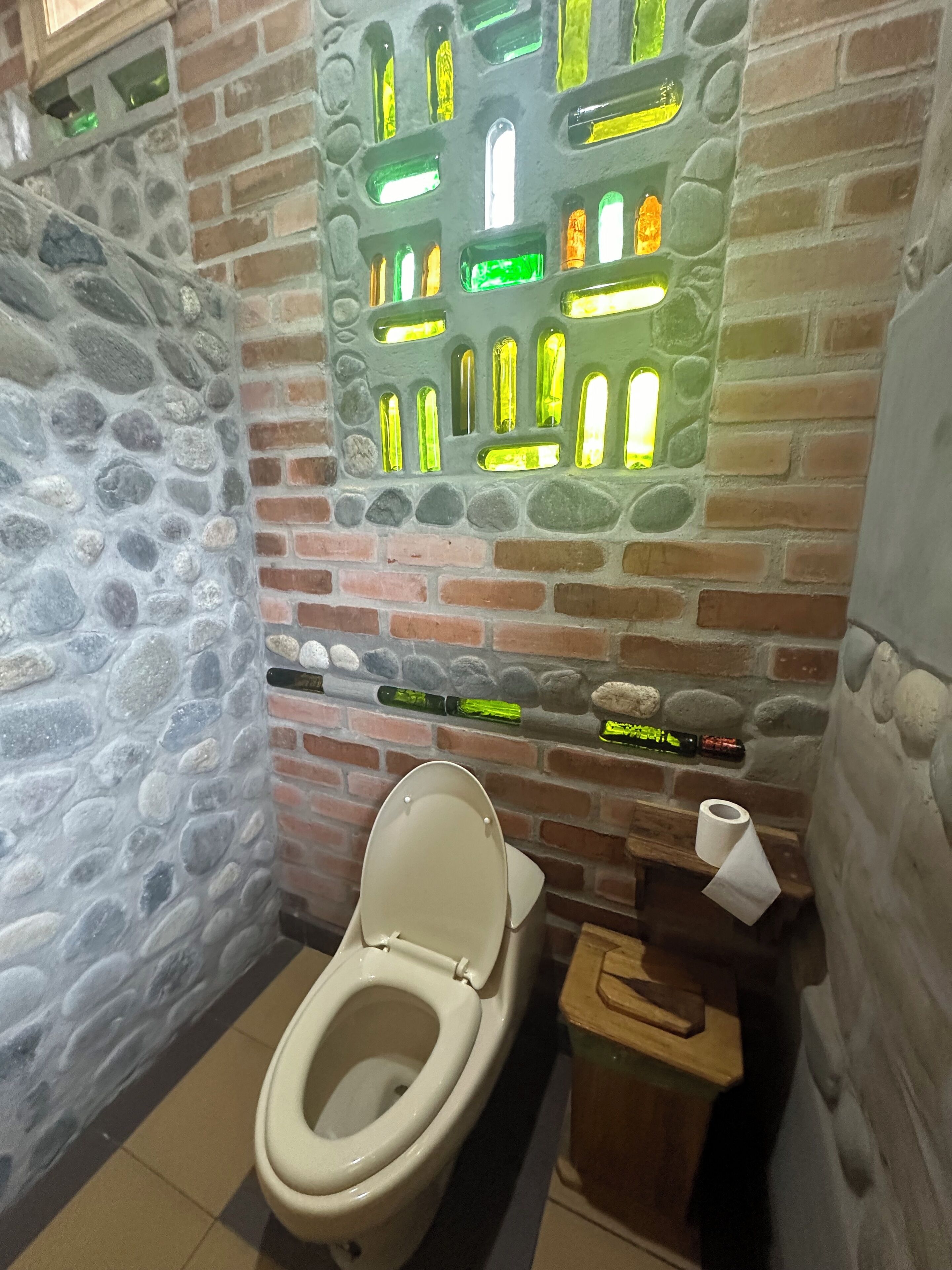 Une salle de bain avec un mur en pierre, des toilettes et une étagère avec des bouteilles.