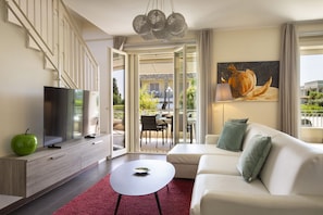 A modern living room with a flat-screen TV, a white sofa, a round coffee table, and a red rug. - Apartment Delphine with shared Pool (Castelnuovo del Garda)