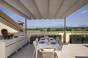 Una terraza con mesa para cuatro, cocina al aire libre y plantas en macetas.