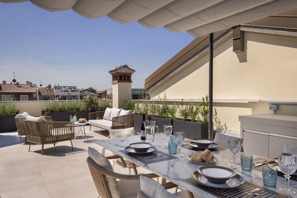 A rooftop terrace with a dining table set for four, outdoor furniture, and a view of the cityscape. - Apartment Delphine with shared Pool (Castelnuovo del Garda)