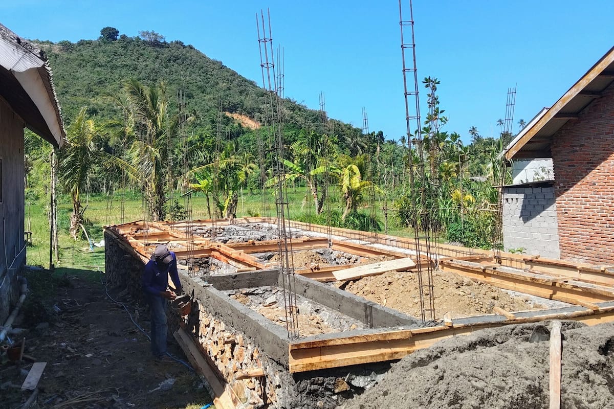 A construction site with a partially built structure, a worker, and a hilly landscape in the background.