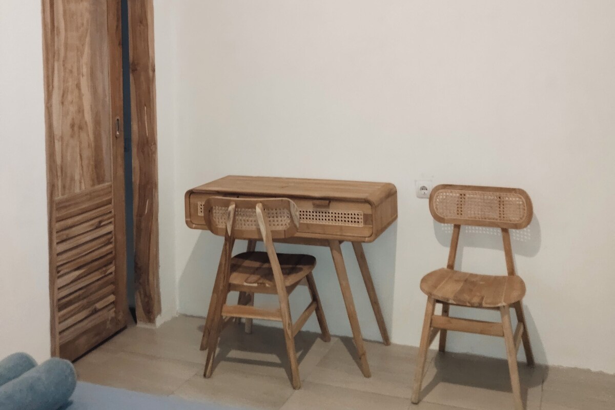 A room with a wooden wardrobe, a desk with a chair, and a bed.