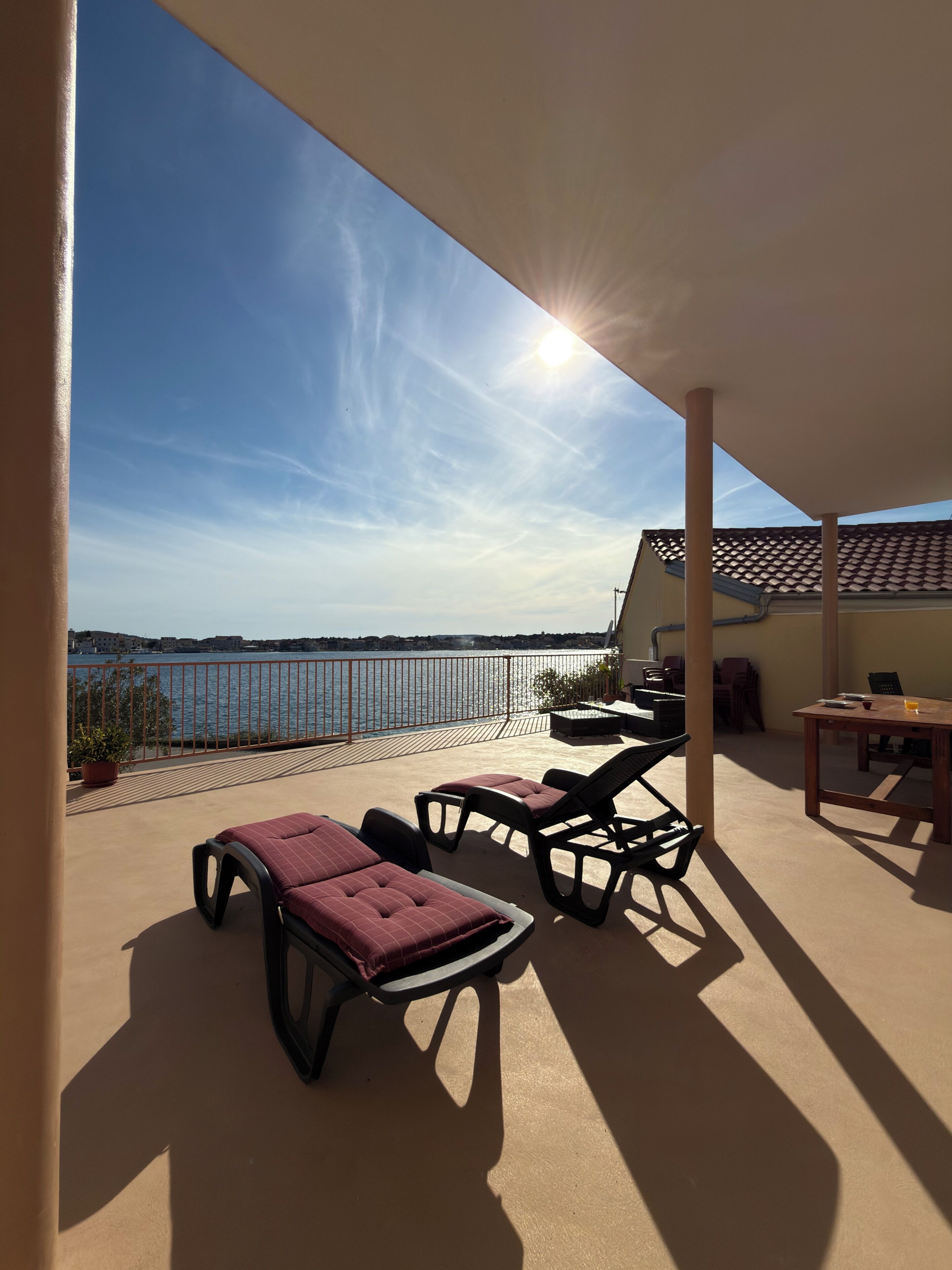 Ein Balkon mit Liegestühlen, einem Tisch und Blick aufs Meer.